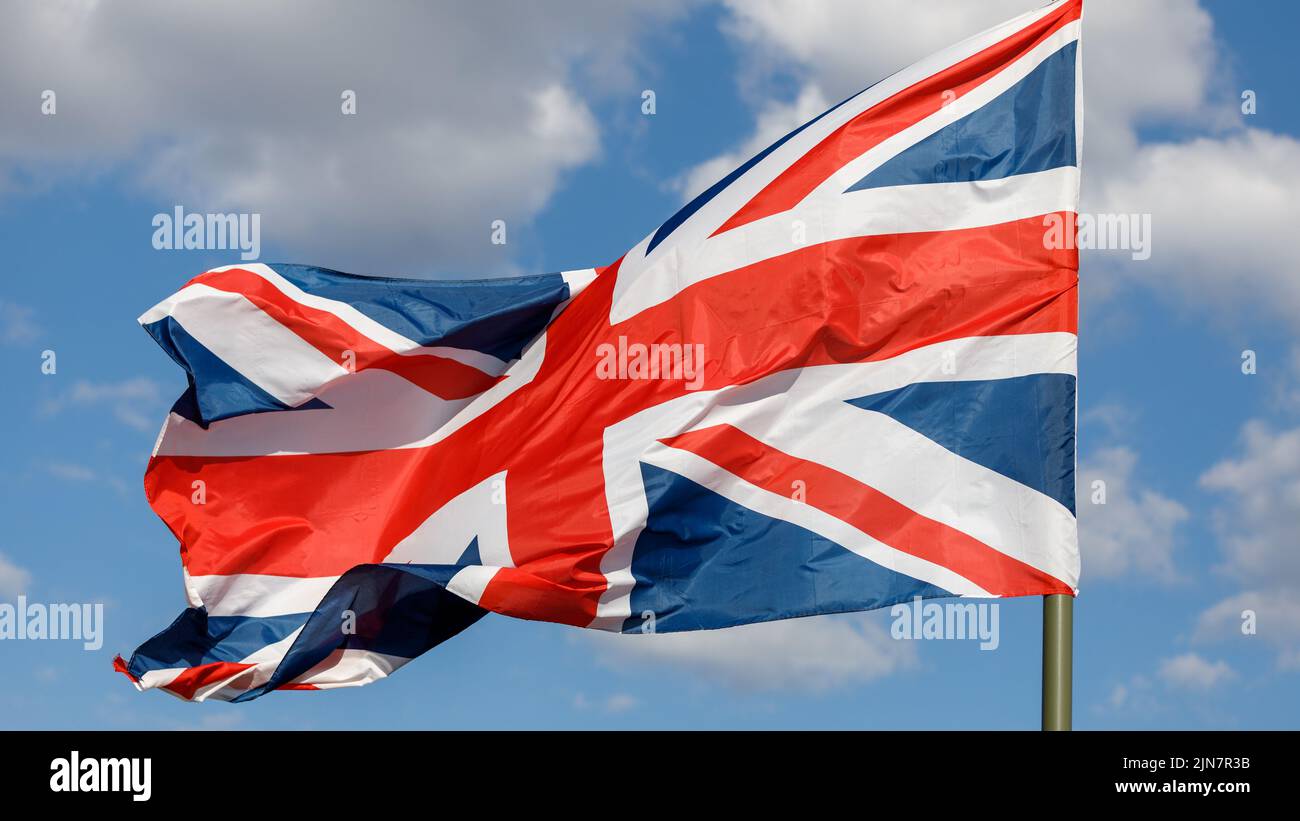 Union Jack flag on a blue sky background futtering in the wind. The ...