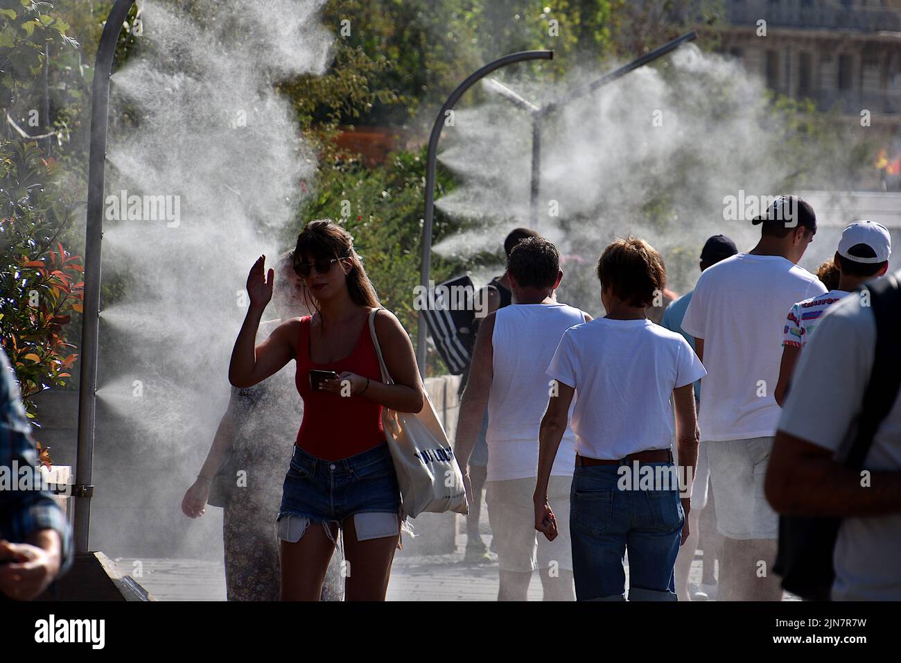 People pass under water sprayers in PACA. To cope with the high temperatures and a probable heat wave, the City of Marseille has installed misters on the quays of the Old Port so that passersby can cool off. Stock Photo