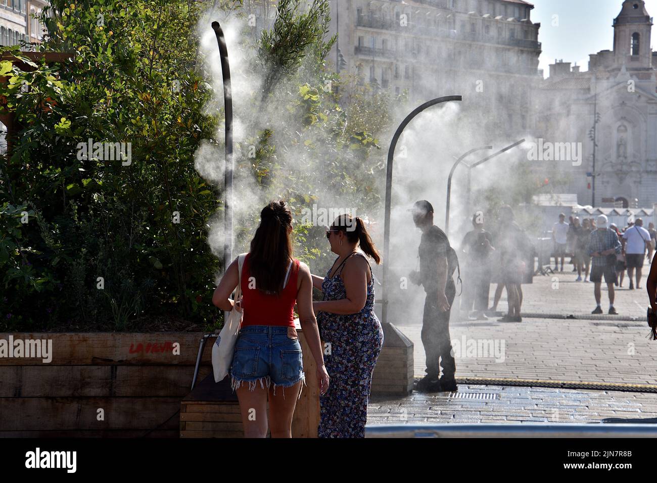 People pass under water sprayers in PACA. To cope with the high temperatures and a probable heat wave, the City of Marseille has installed misters on the quays of the Old Port so that passersby can cool off. Stock Photo