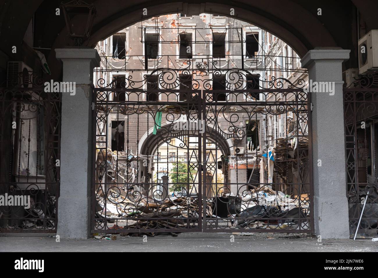 A decorative wrought-iron fence in the courtyard of the damaged building. Destroyed building in historical downtown in Kharkiv, Ukraine - 1 Aug 2022 Stock Photo
