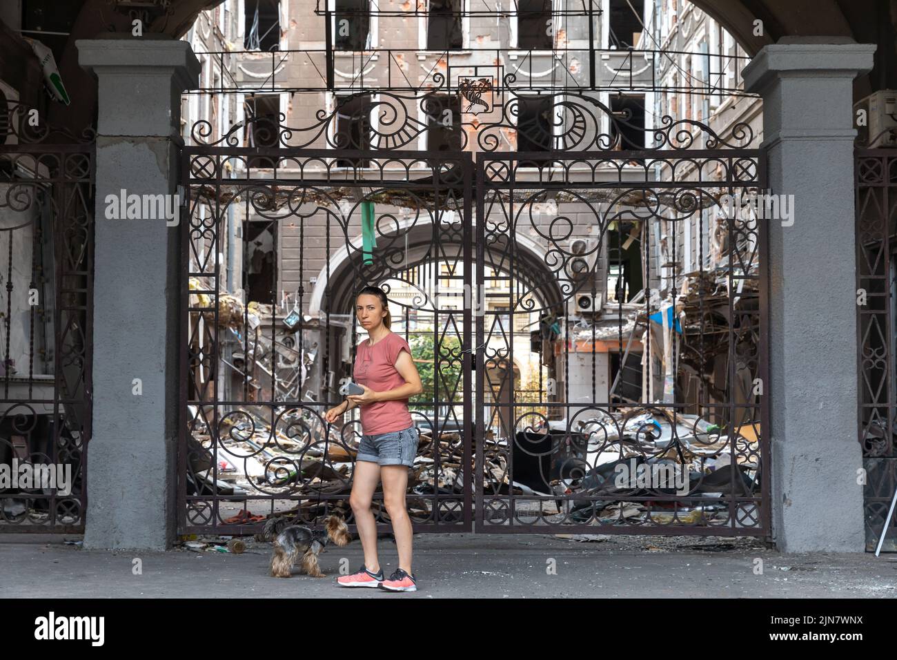 A young lady with a dog seen near the entrance to the courtyard of a damaged house. Destroyed building in historical downtown in Kharkiv, Ukraine - 1 Aug 2022 (Photo by Mykhaylo Palinchak / SOPA Images/Sipa USA) Stock Photo