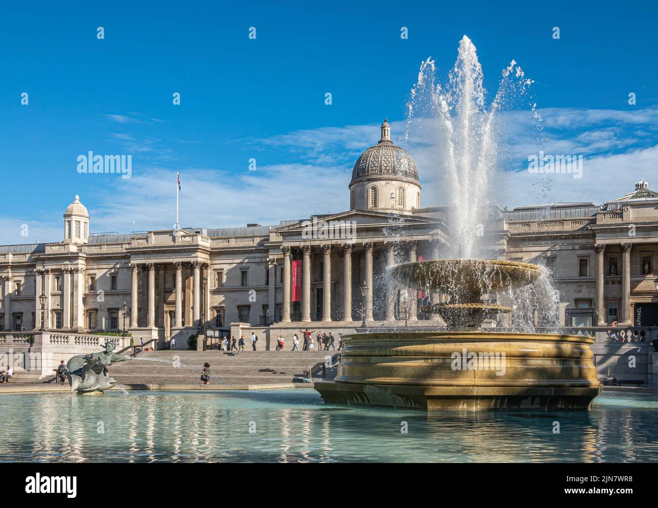 London, UK- July 4, 2022: Trafalgar Square. Wide view on Full blowing water Jellycoe fountain with National Gallery building in back under blue clouds Stock Photo
