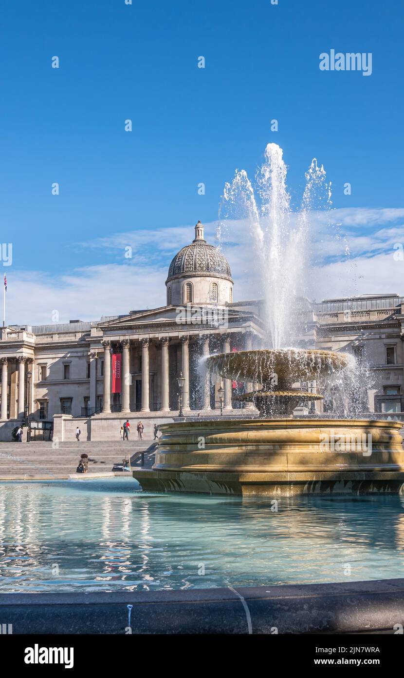 London, UK- July 4, 2022: Trafalgar Square. Full blowing water Jellycoe fountain with National Gallery building in back under blue cloudscape. Stock Photo