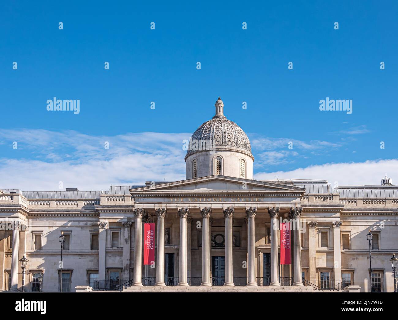 London, UK- July 4, 2022: Trafalgar Square. Central part with dome and pediment of National Gallery building under blue cloudscape. Red banners add co Stock Photo