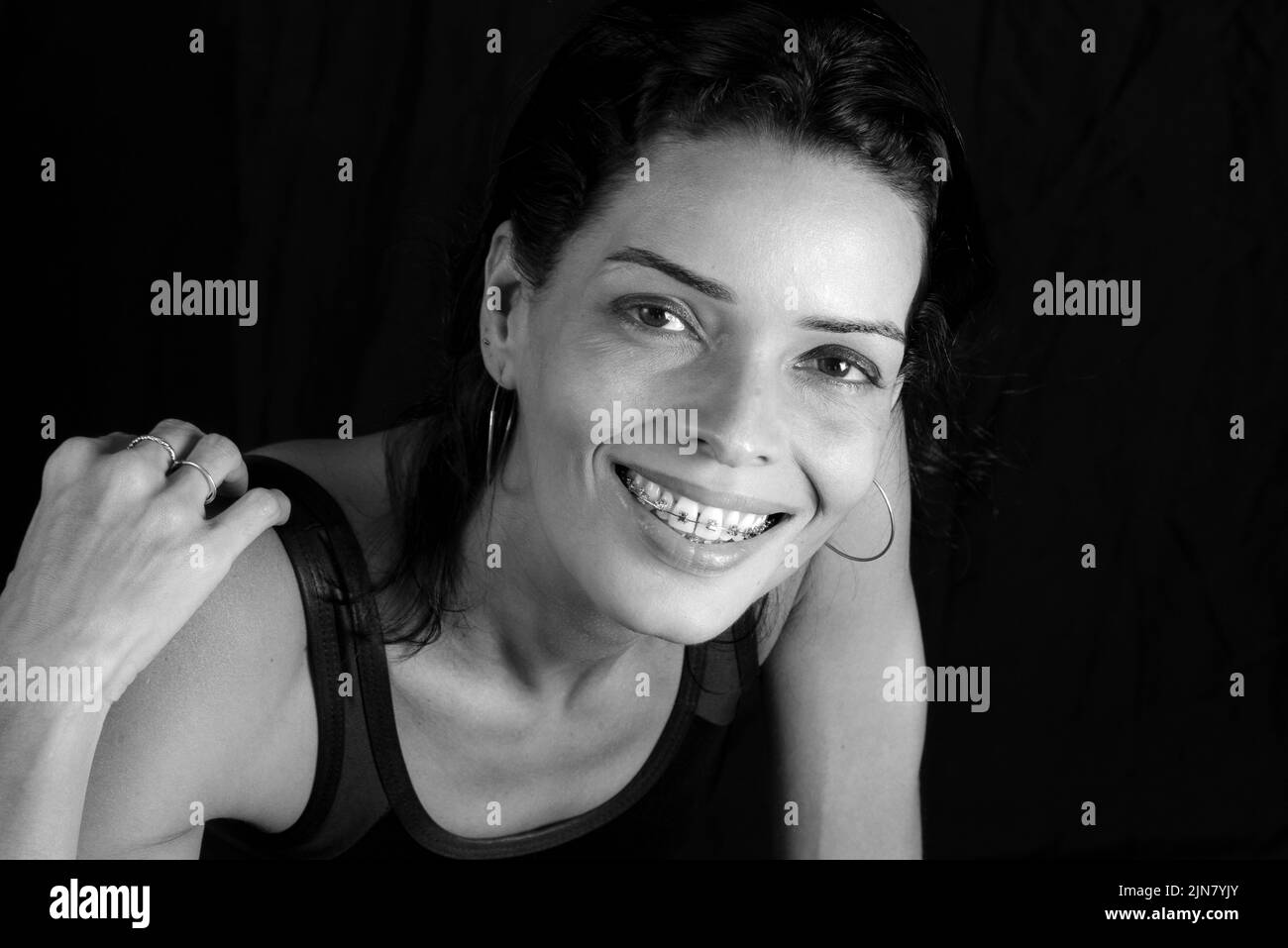 Studio Portrait in black and white of young woman in black t-shirt smiling at camera against black studio background. Salvador, Brazil. Stock Photo