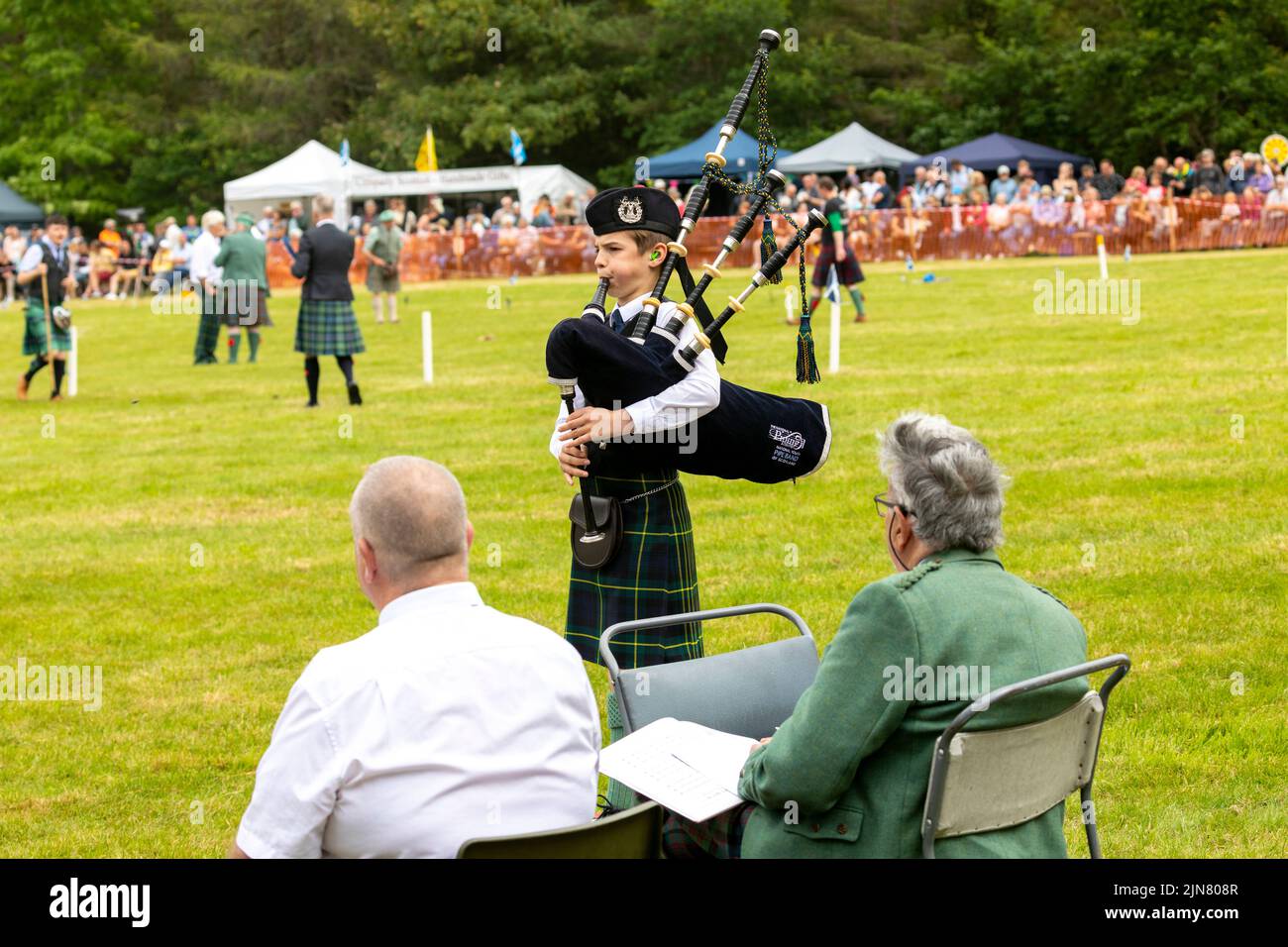 Tomintoul Highland games 2022, young boy plays the bagpipes and is judged by two elderly judges, Scotland,UK,summer 2022 Stock Photo