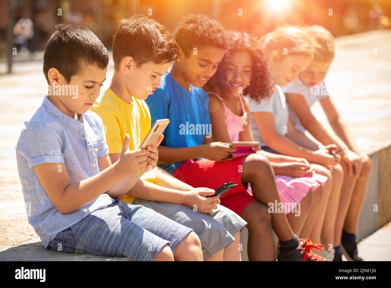 Children chatting on their smartphone, sitting on parapet Stock Photo ...