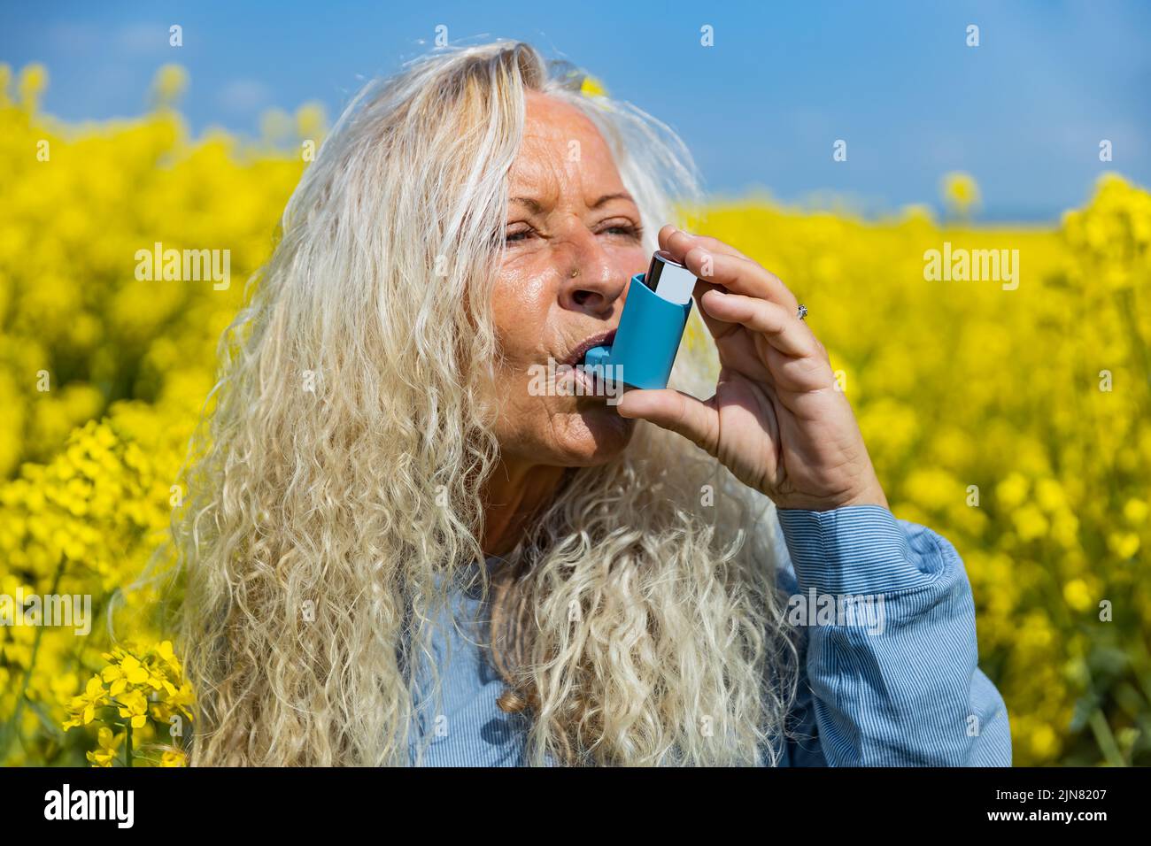 Elderly woman using an asthma metered dose inhaler in a blooming canola field Stock Photo