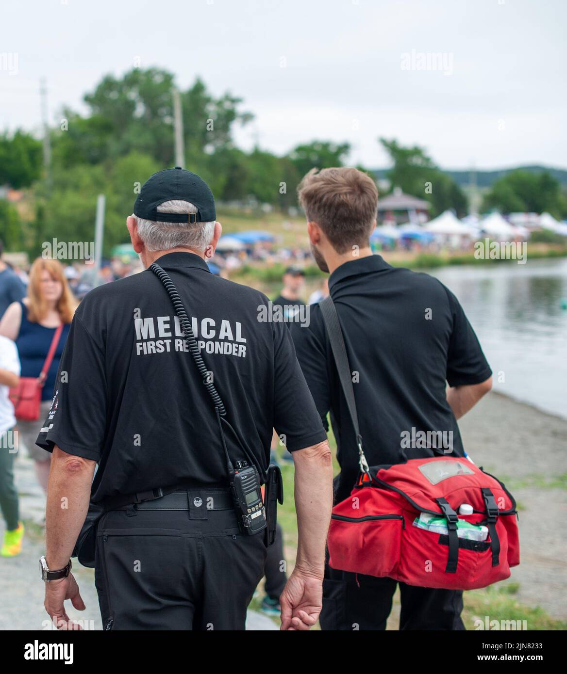 Two adult male medical first responders walking on a road among a crowd of people. Both are wearing black and grey colored paramedic uniforms. Stock Photo