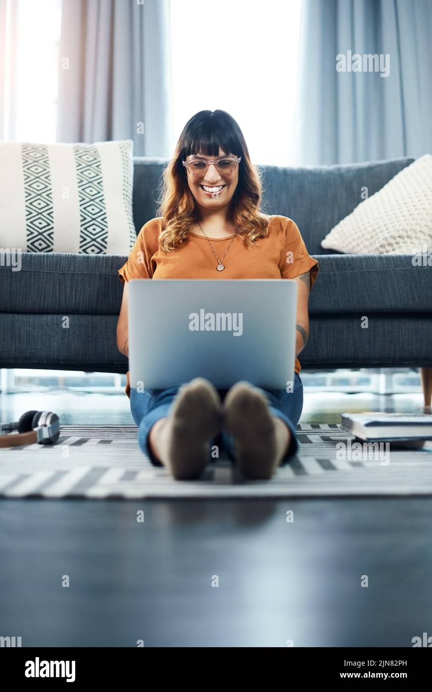 Heres something thatll keep me busy. a young woman using her laptop while relaxing at home. Stock Photo