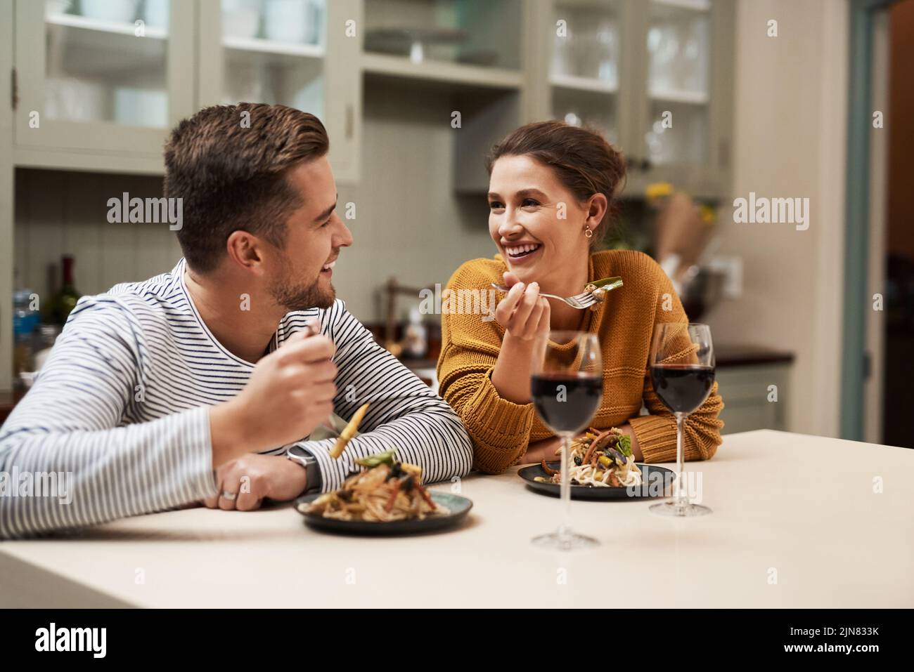 Who doesnt love a home cooked meal. an affectionate young couple smiling at each other while enjoying dinner in their kitchen at home. Stock Photo