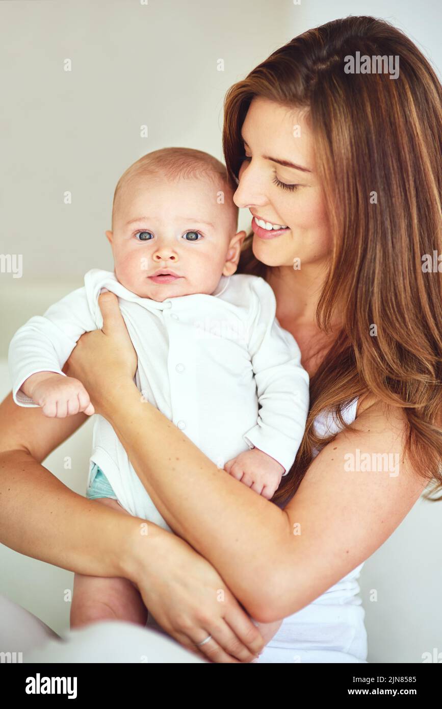 Beautiful family portrait of mother and baby boy hugging, bonding at home, carefree and loving. Smiling, cheerful parent embracing her newborn Stock Photo