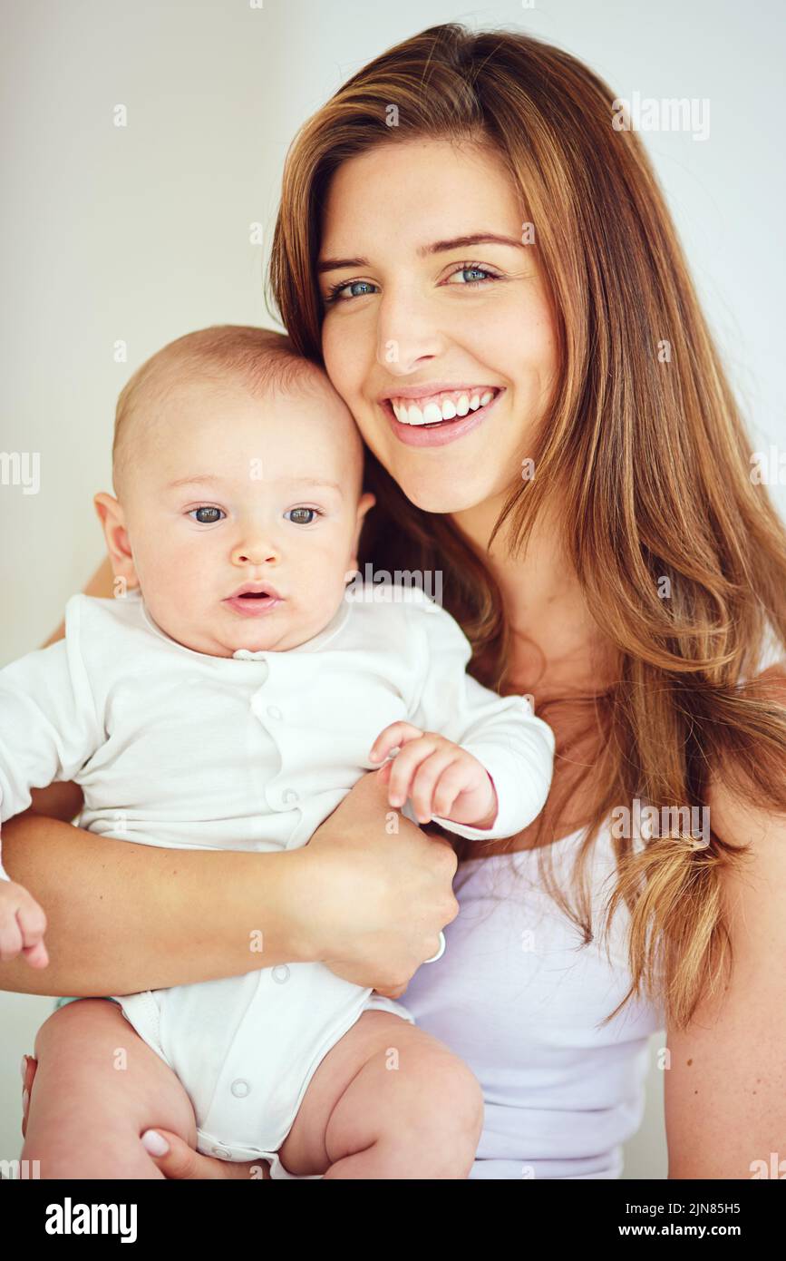 A beautiful, loving and caring mother holding baby, smiling and looking happy with new born. Single blonde parent or young mom showing love and care Stock Photo