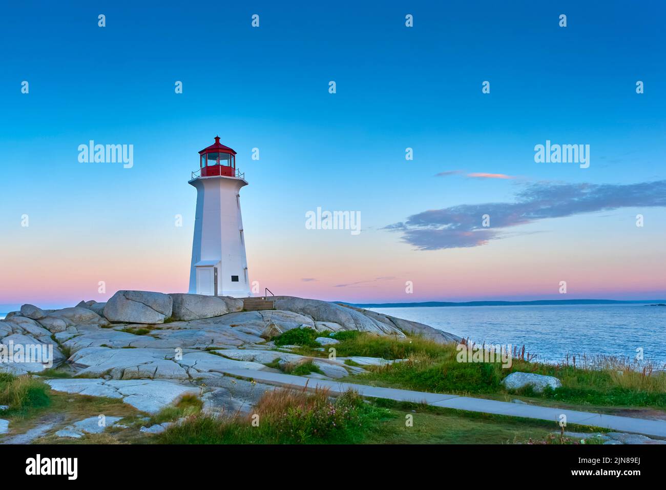 Photograph of the iconic Peggy's Cove lighthouse taken at sunrise on a beautiful summer morning.. Stock Photo