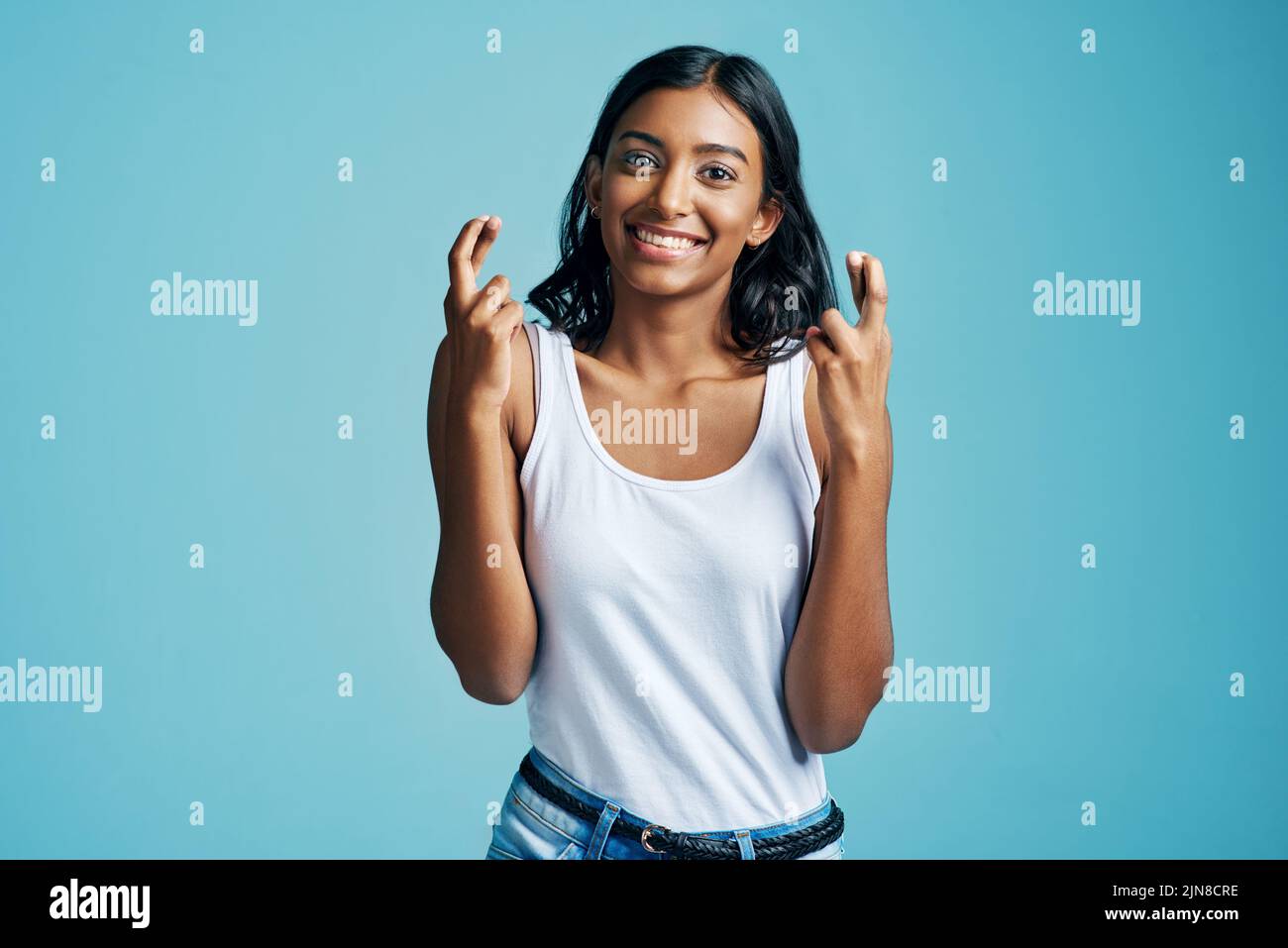 Heres hoping. Studio portrait of a beautiful young woman crossing her fingers against a blue background. Stock Photo