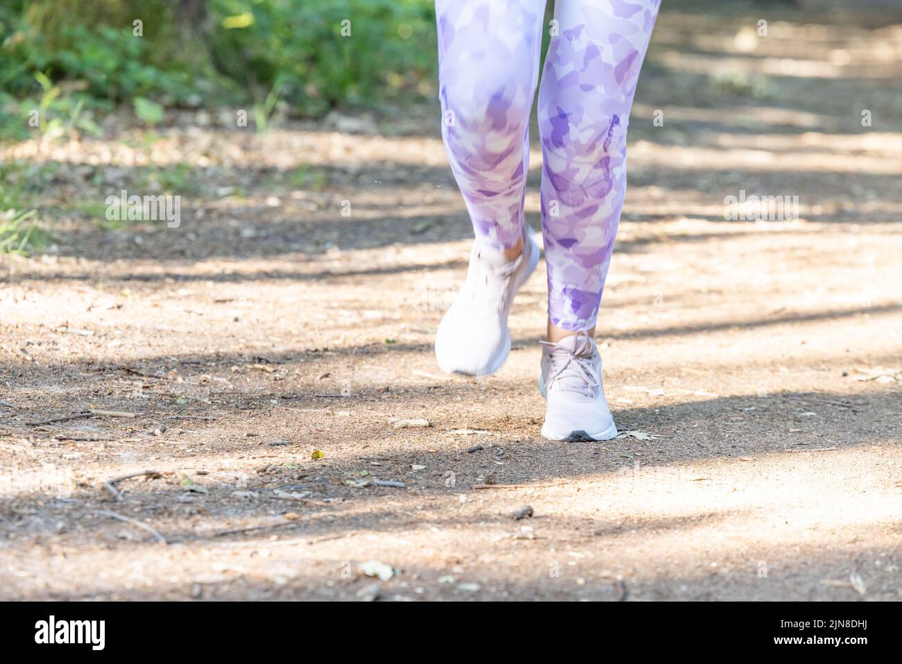 Close up of the feet of young fitness woman running at forest trail in the sun, Exercising outdoors is healthy for active lifestyle runners. Autumn trail run woman running in nature, Outdoor jog. High quality photo Stock Photo