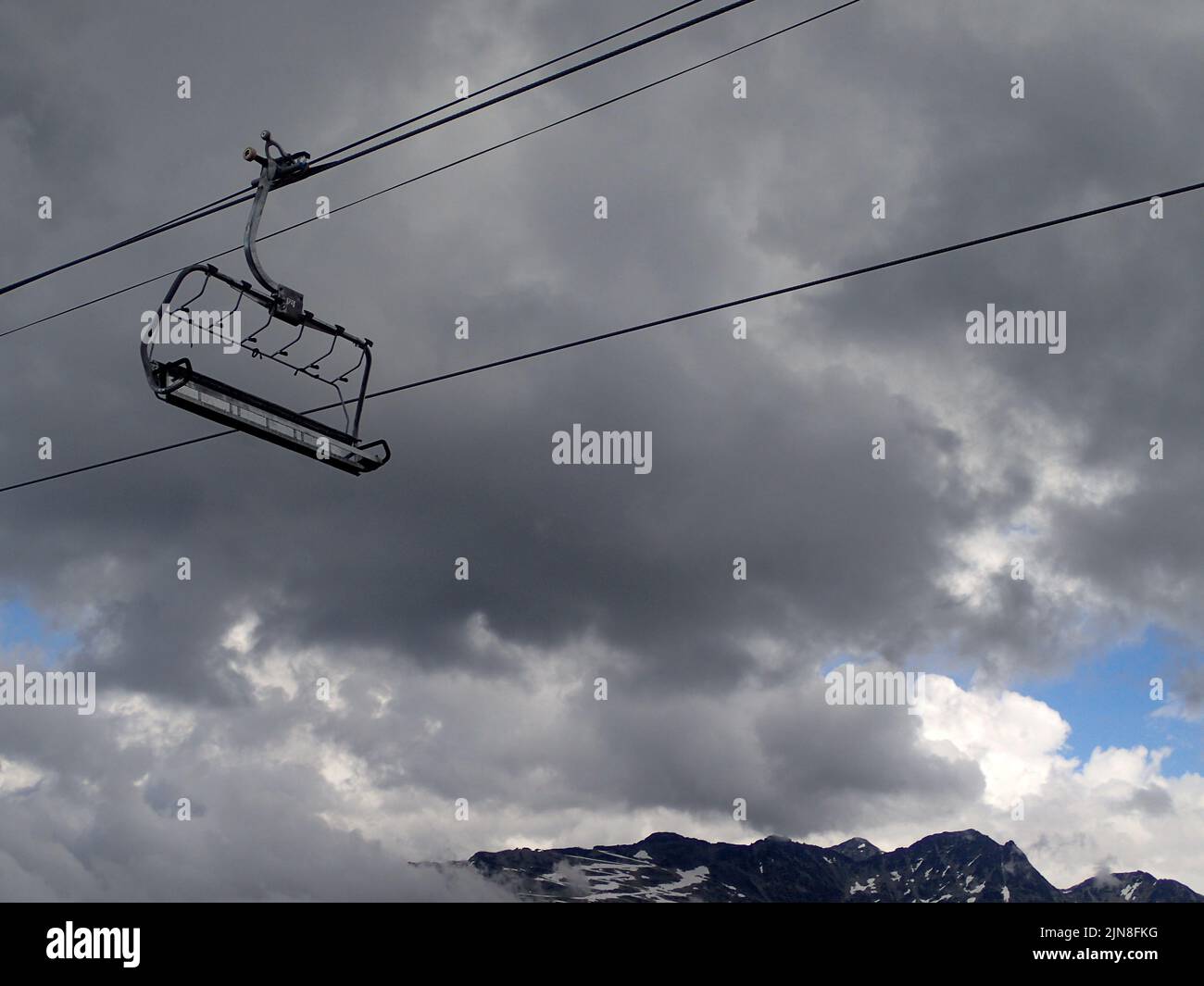 A single chairlift hanging on a rope outlined against a cloudy sky ...