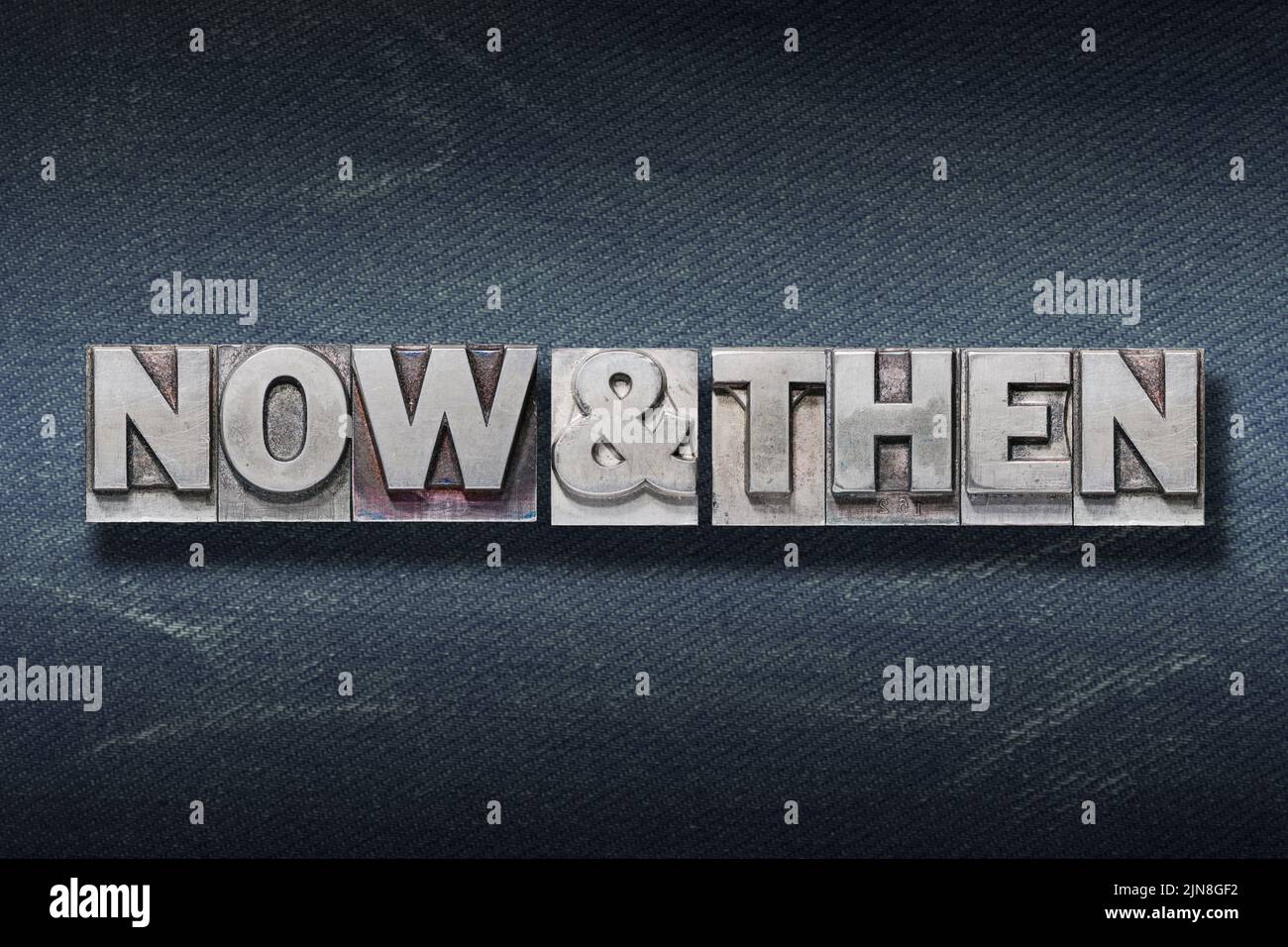 now and then phrase made from metallic letterpress on dark jeans background Stock Photo