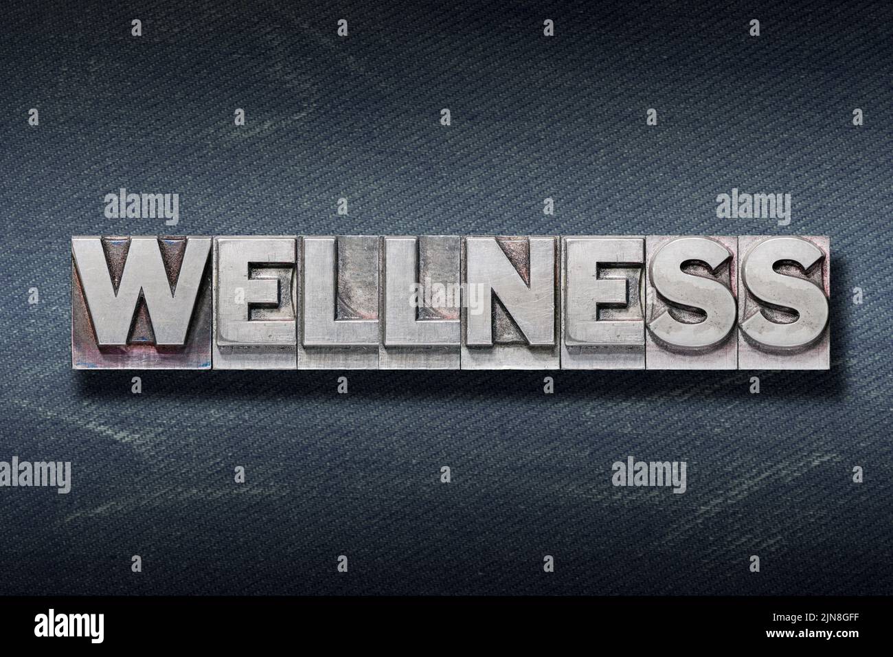 wellness word made from metallic letterpress on dark jeans background Stock Photo