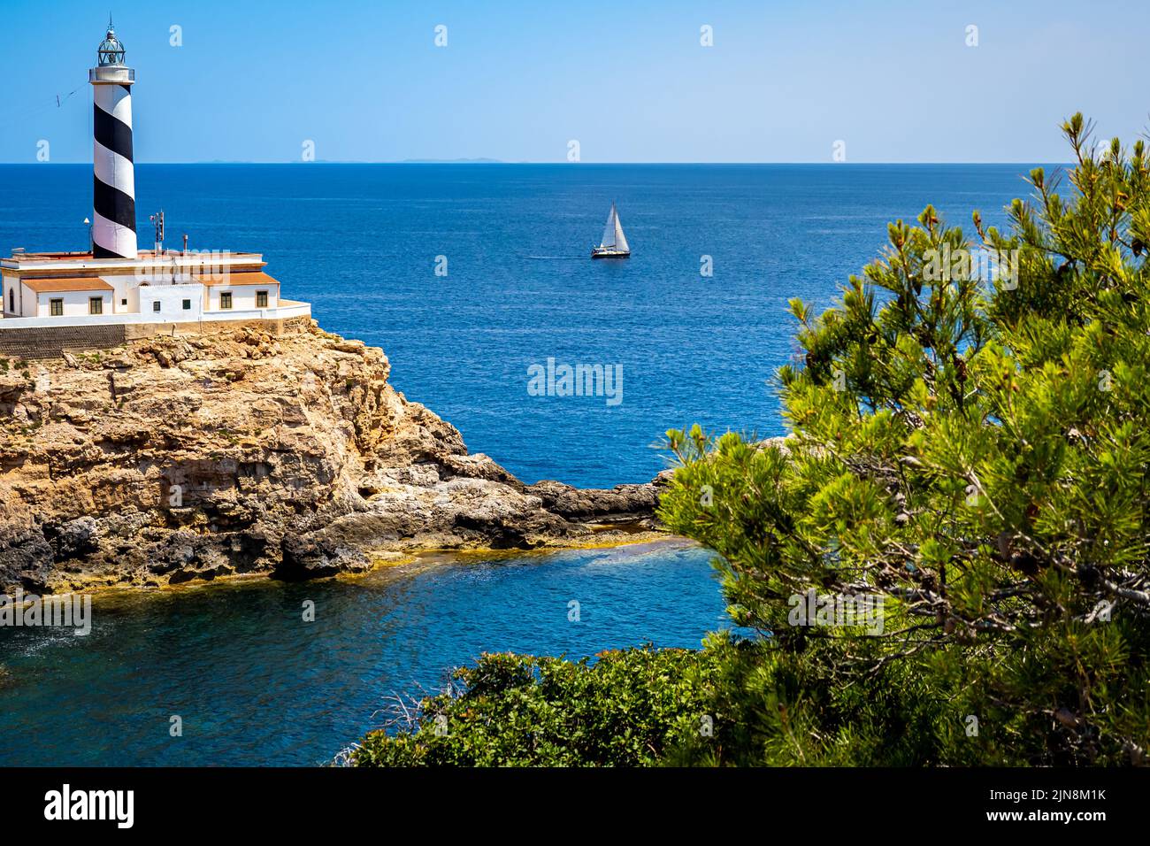 Idyllic Mallorca bay Es Mular with the lighthouse Faro de Cala Figuera in front of a sailboat on the mediterranean sea and islands of Cabrera. Stock Photo