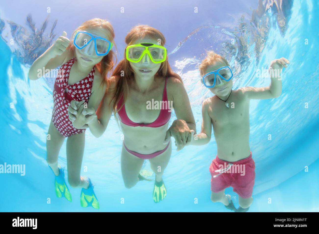 Happy people dive underwater with fun. Funny photo of mother, kids in snorkeling masks in aqua park swimming pool. Family lifestyle. Stock Photo