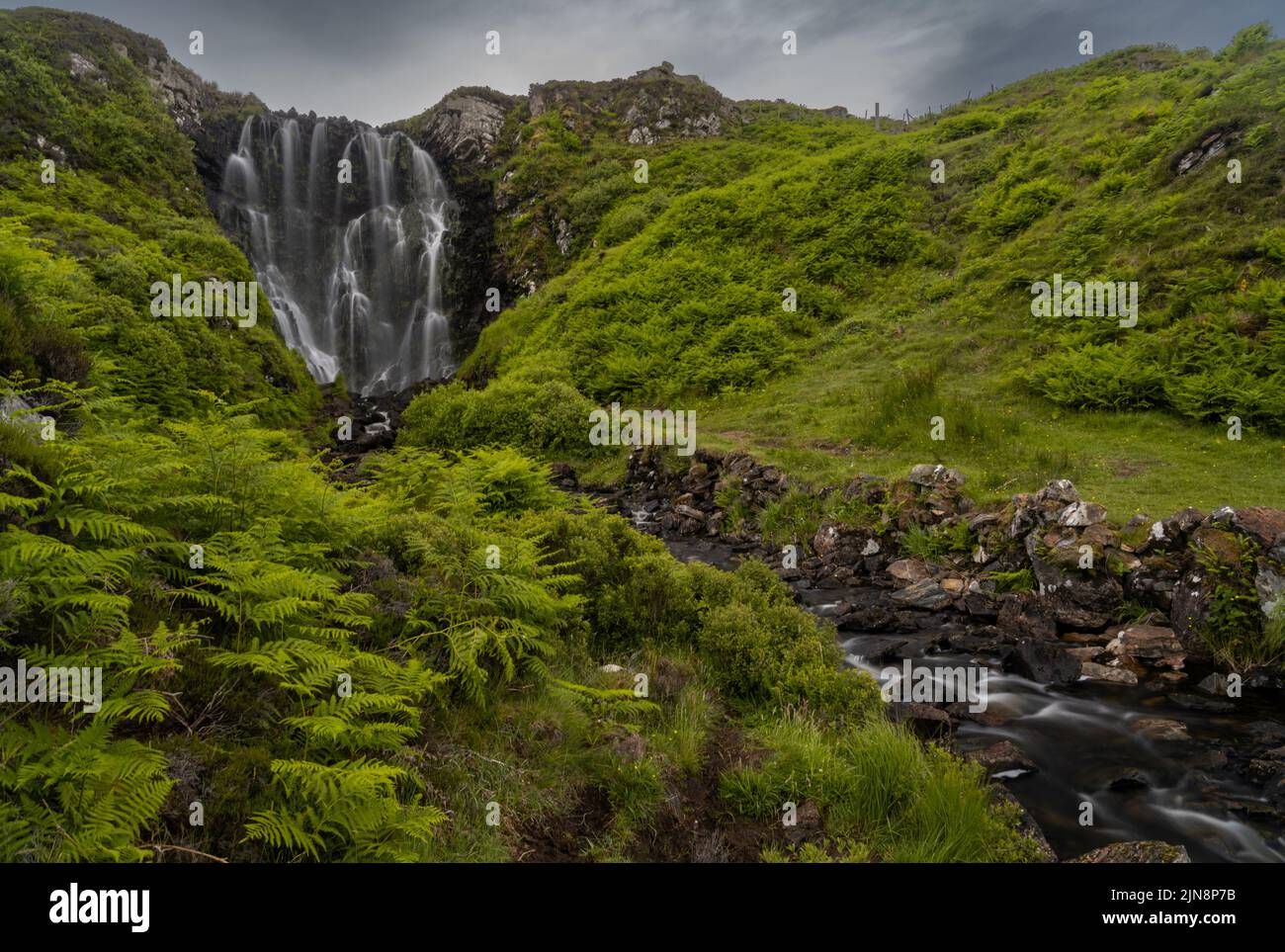 A view of the Clashniesse Waterfall in the Scottish Highlands in high summer with lush green ferns in the foreground Stock Photo