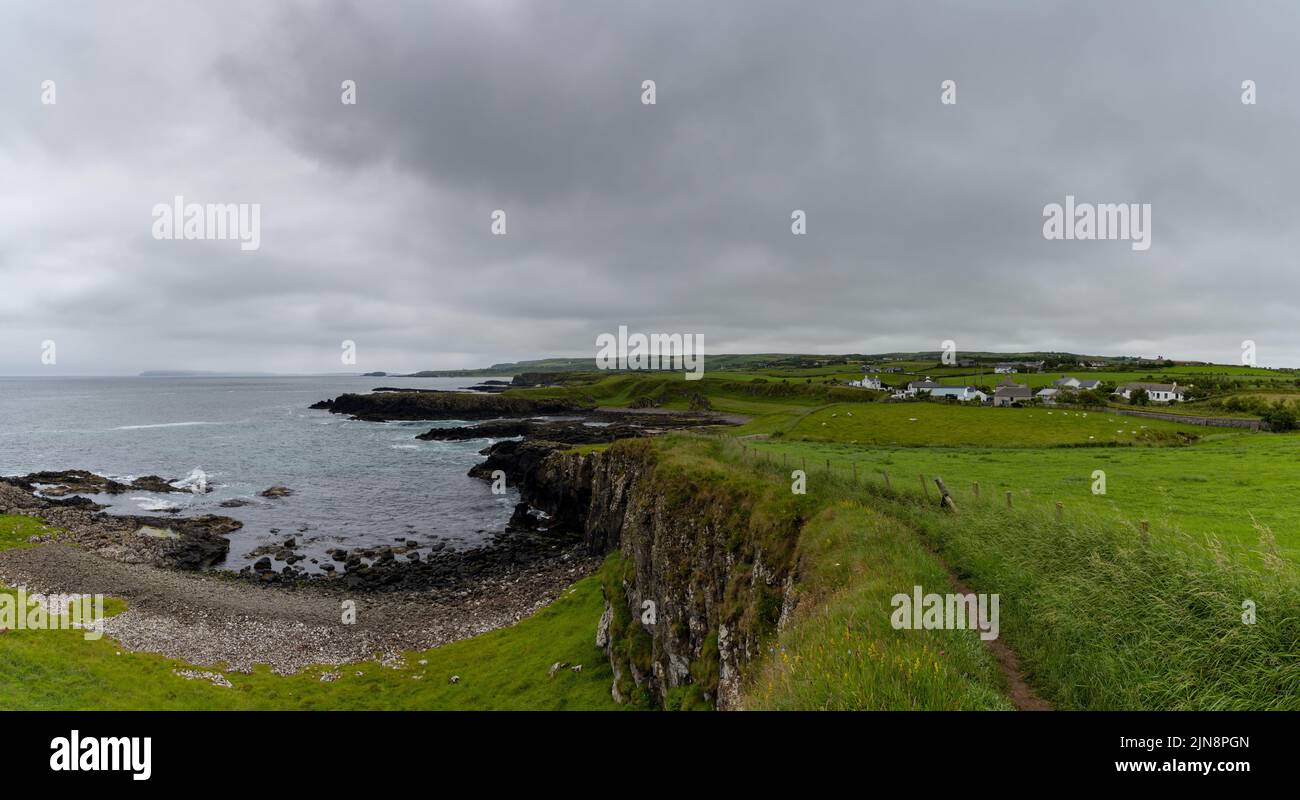panorama view of rugged green coastline with a hiking trail in the foreground under an overcast sky Stock Photo