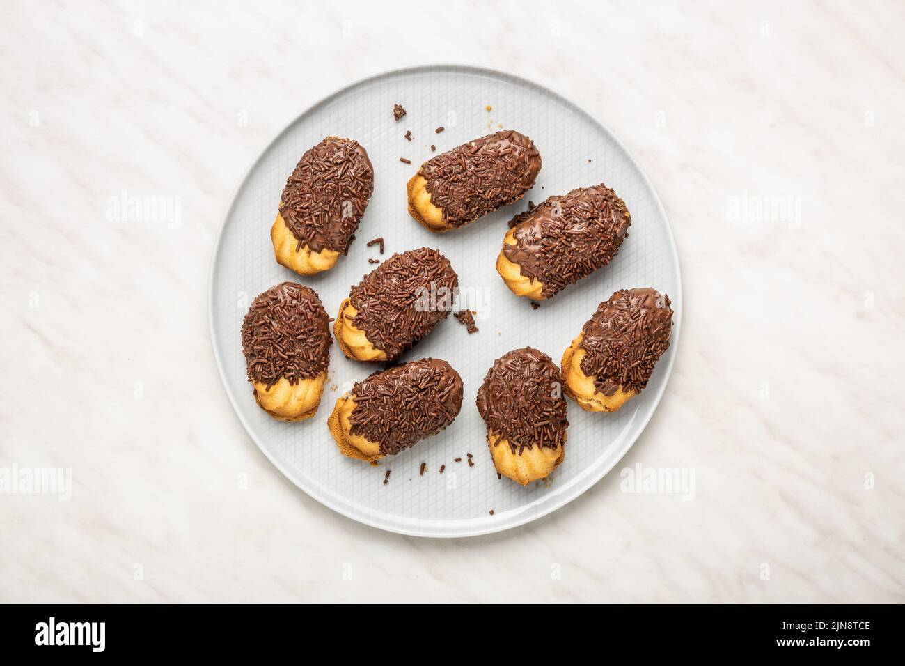 Petit fours with chocolate sprinkles on kitchen table. Mini chocolate dessert on a plate. Top view. Stock Photo