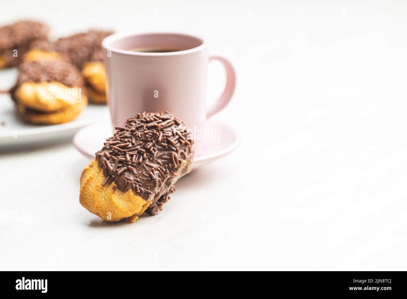 Petit fours with chocolate sprinkles. Mini chocolate dessert and a coffee cup on white kitchen table. Stock Photo