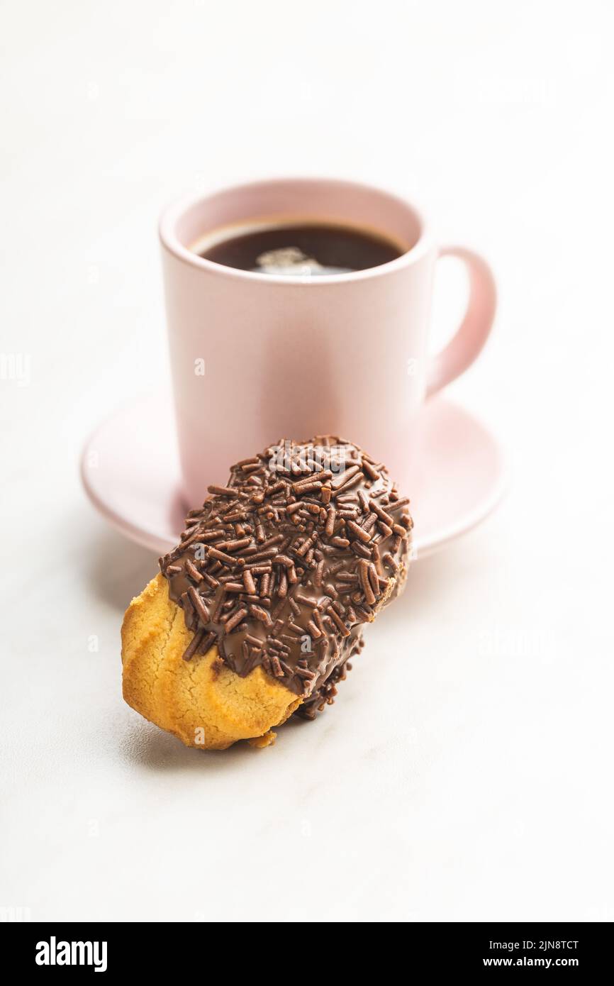 Petit fours with chocolate sprinkles. Mini chocolate dessert and a coffee cup on white kitchen table. Stock Photo