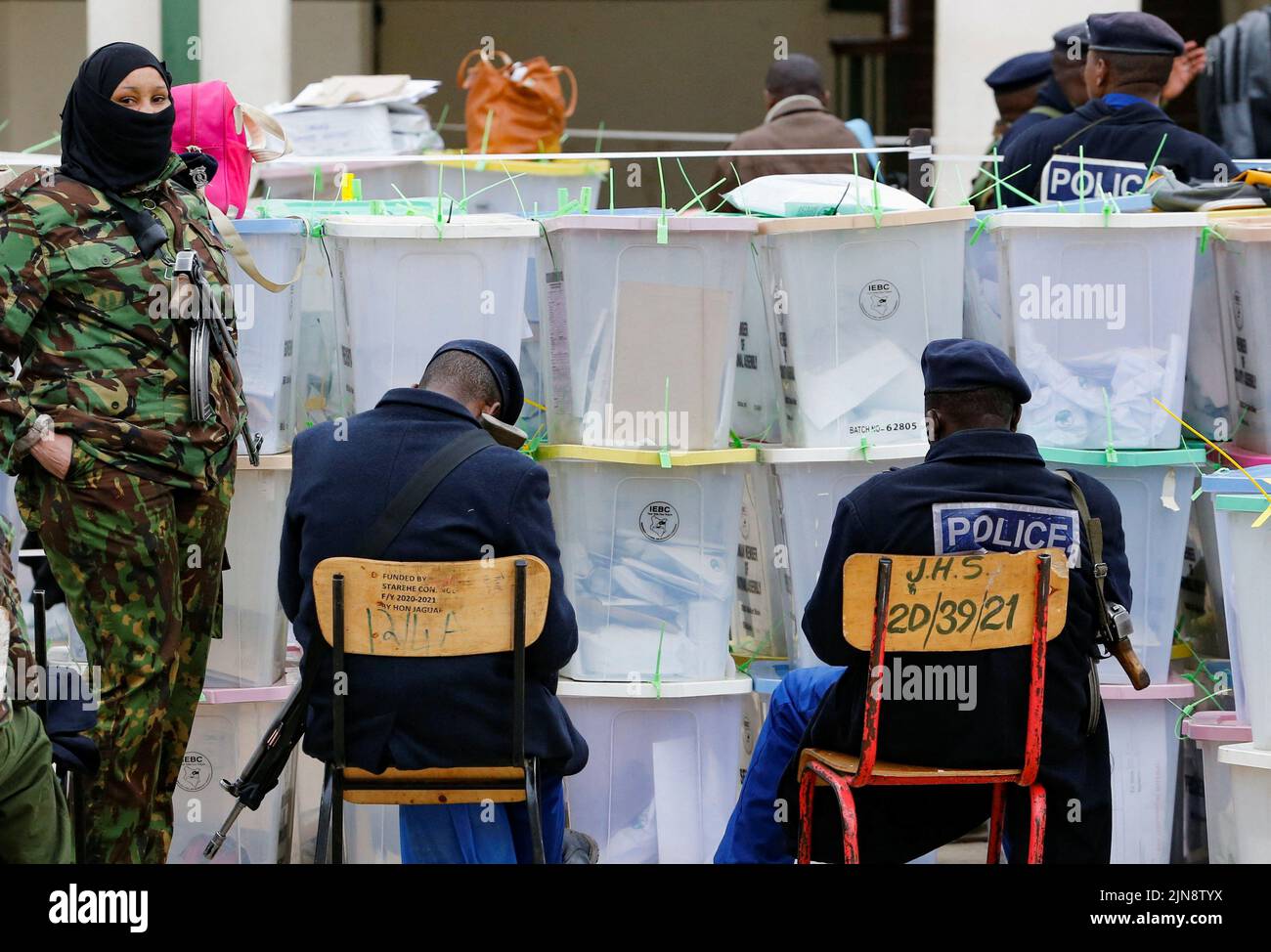 A police officer stands guard as her colleagues rest while guarding the sealed ballot boxes containing electoral materials at an Independent Electoral and Boundaries Commission (IEBC) tallying centre after the general election in Nairobi, Kenya August 10, 2022. REUTERS/Thomas Mukoya Stock Photo