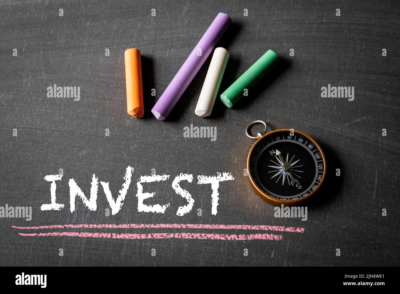 Invest Business Concept. Text and compass on a chalk board. Stock Photo