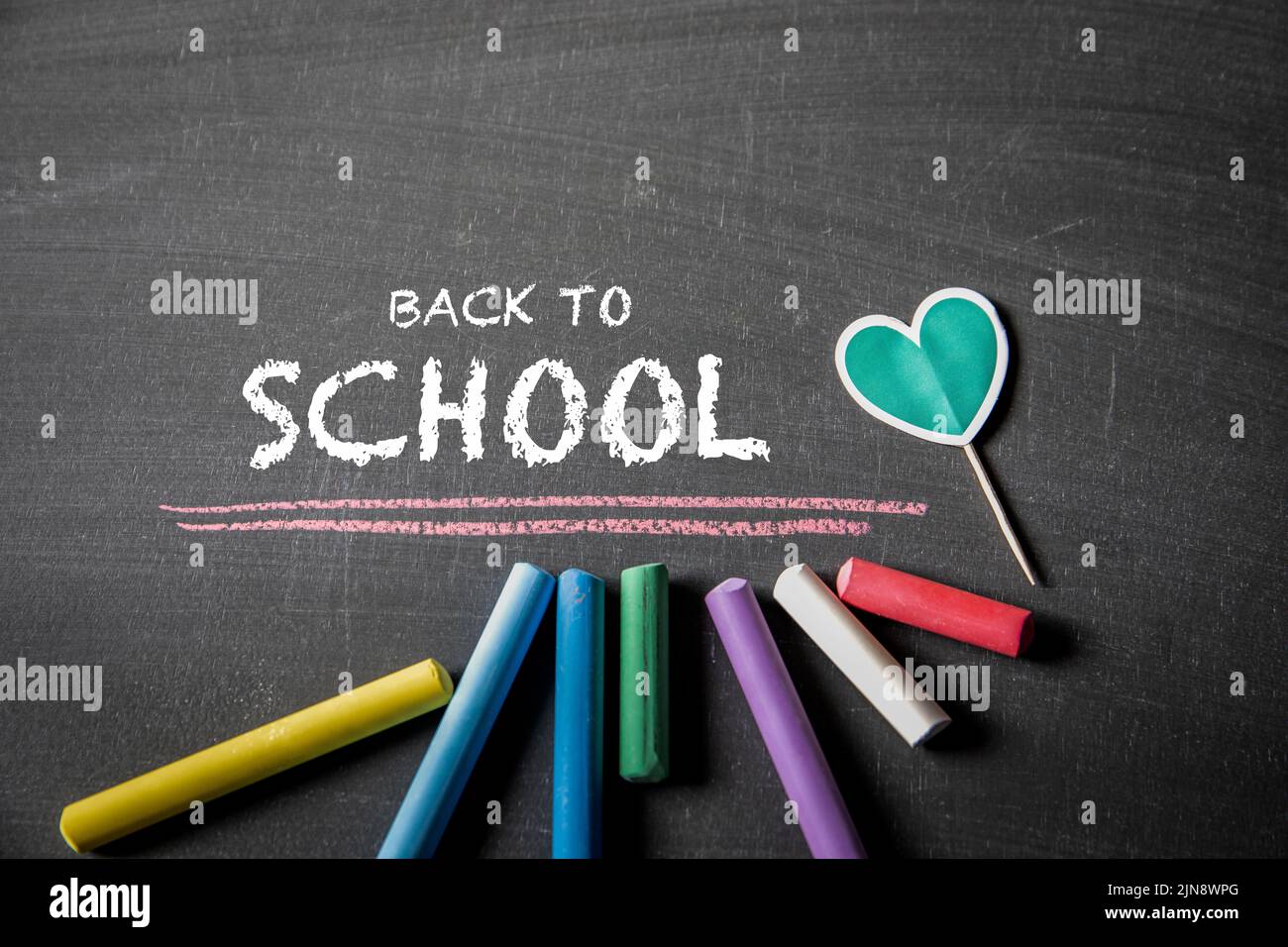 Back to school. Text and colored pieces of chalk on a dark blackboard. Stock Photo