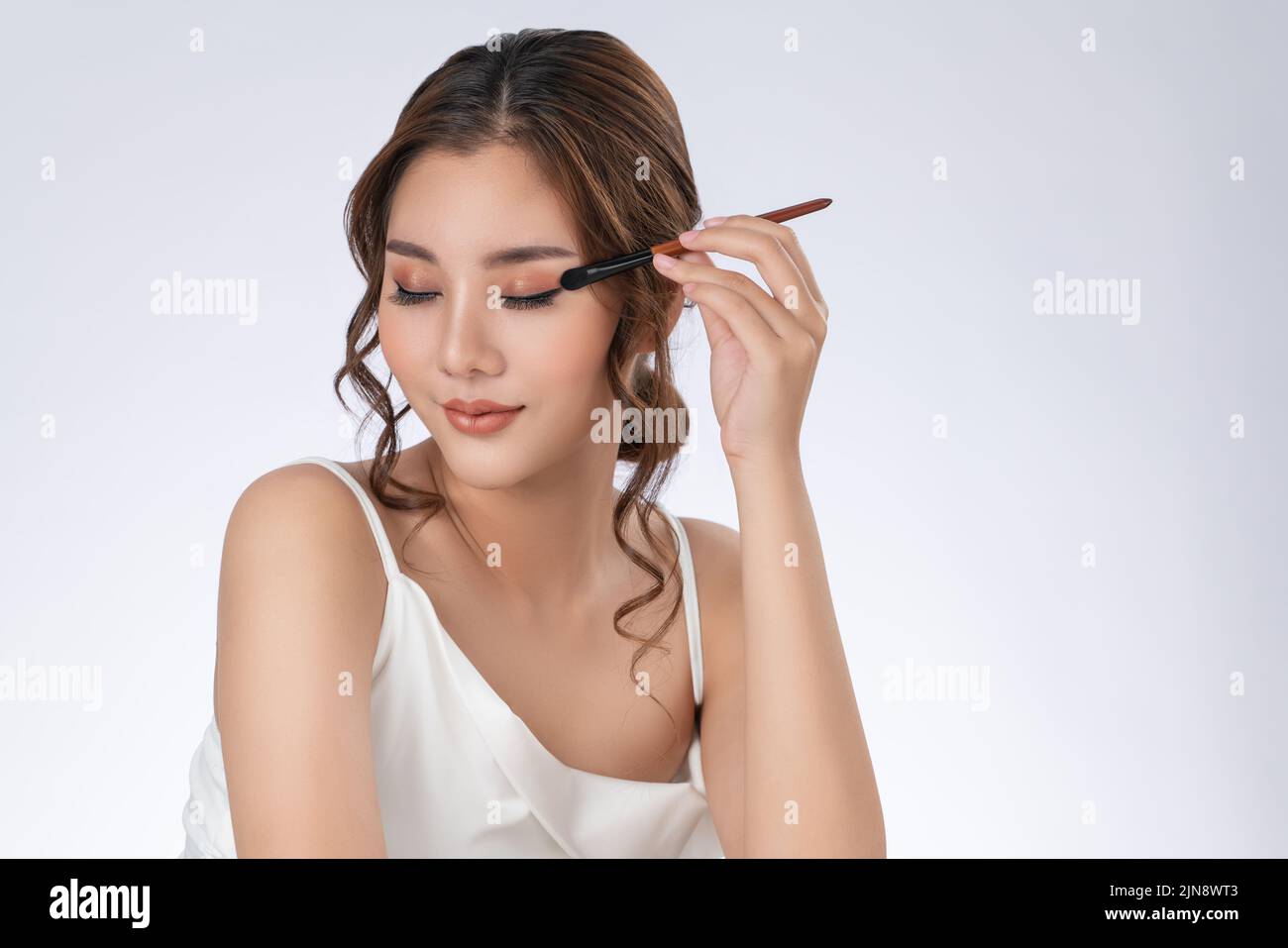 Gorgeous young woman putting black mascara on her long eyelashes with brush. Beauty cosmetic concept. Female model with perfect skin. Stock Photo