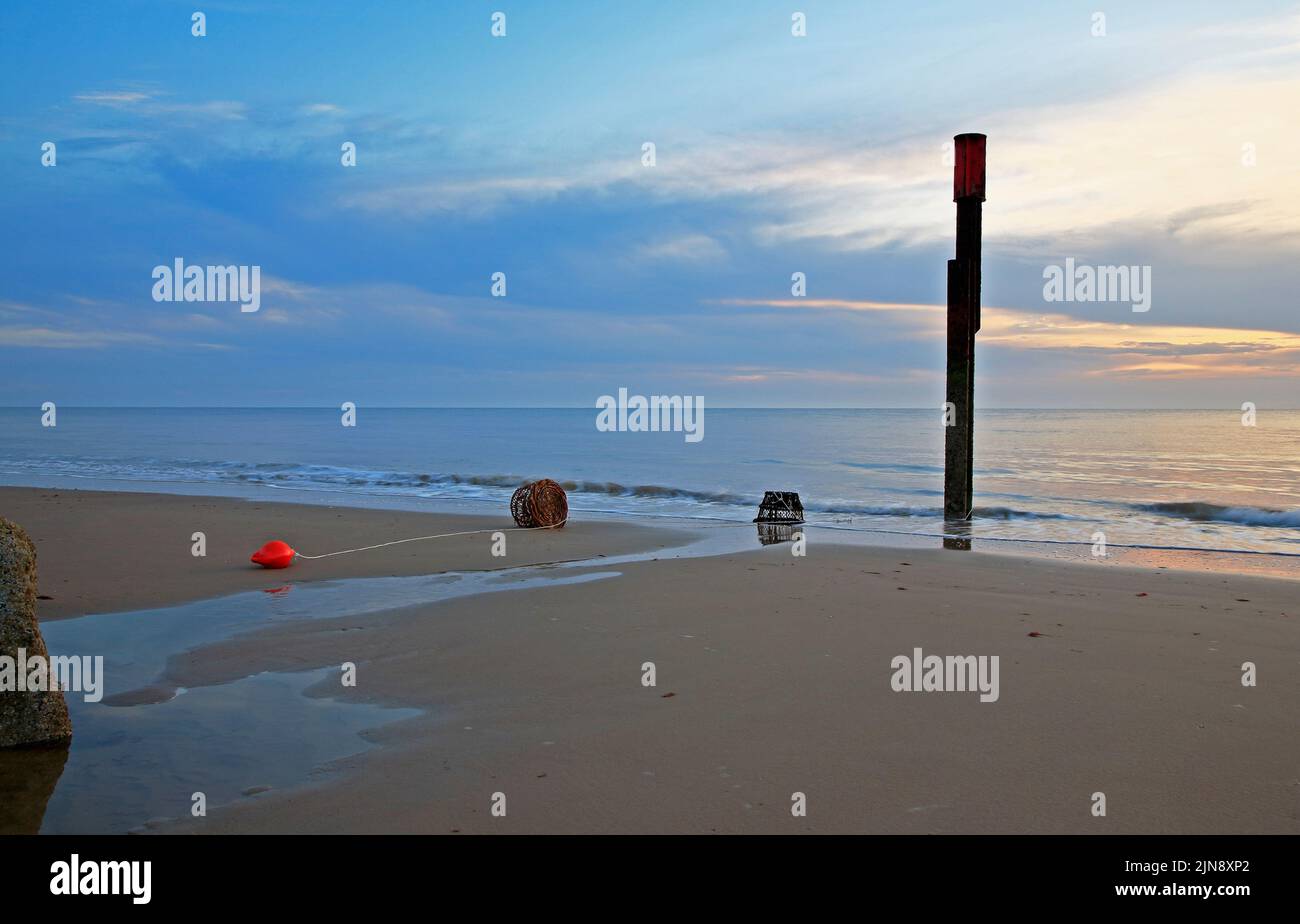 An early morning view of the beach and sea in summer with beached lobster pots and red buoy at Happisburgh, Norfolk, England, United Kingdom. Stock Photo