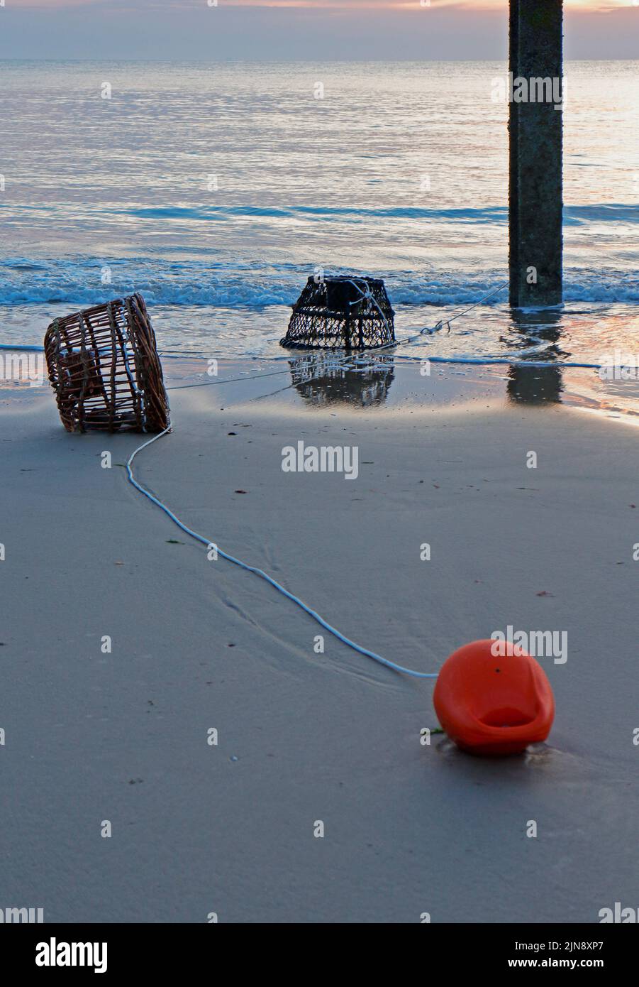 Beached lobster pots and red buoy washed up on the Norfolk coast in summer at Cart Gap, Norfolk, England, United Kingdom. Stock Photo