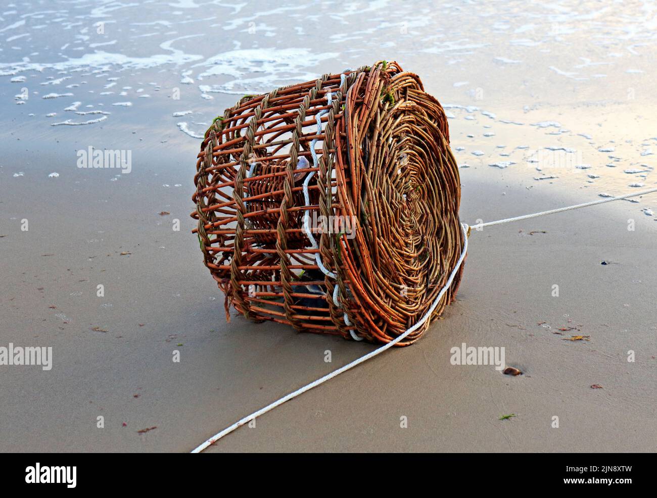 A traditional round wicker lobster or crab pot trap washed up on a Norfolk beach at Cart Gap, Happisburgh, Norfolk, England, United Kingdom. Stock Photo