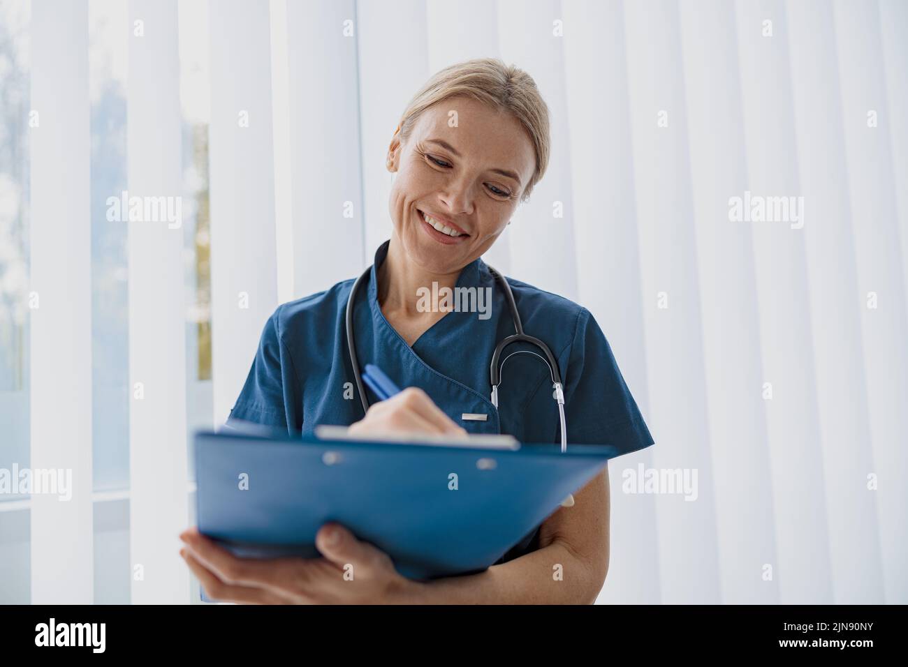 Smiling woman doctor taking notes on clipboard during appointment in medicine center Stock Photo