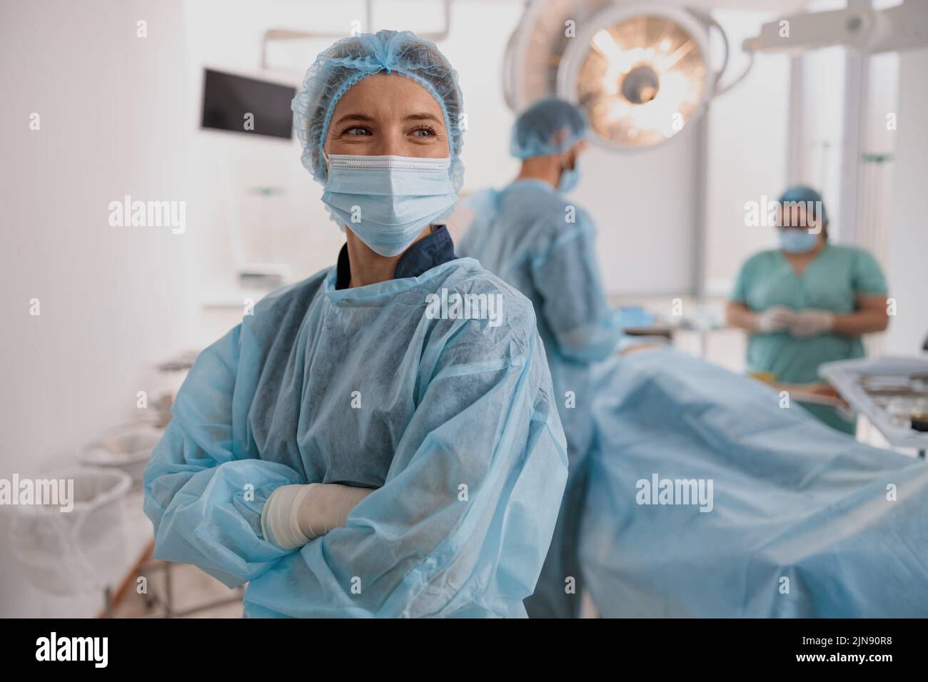 Female surgeon in mask standing in operating room with crossing hands, ready to work on patient Stock Photo