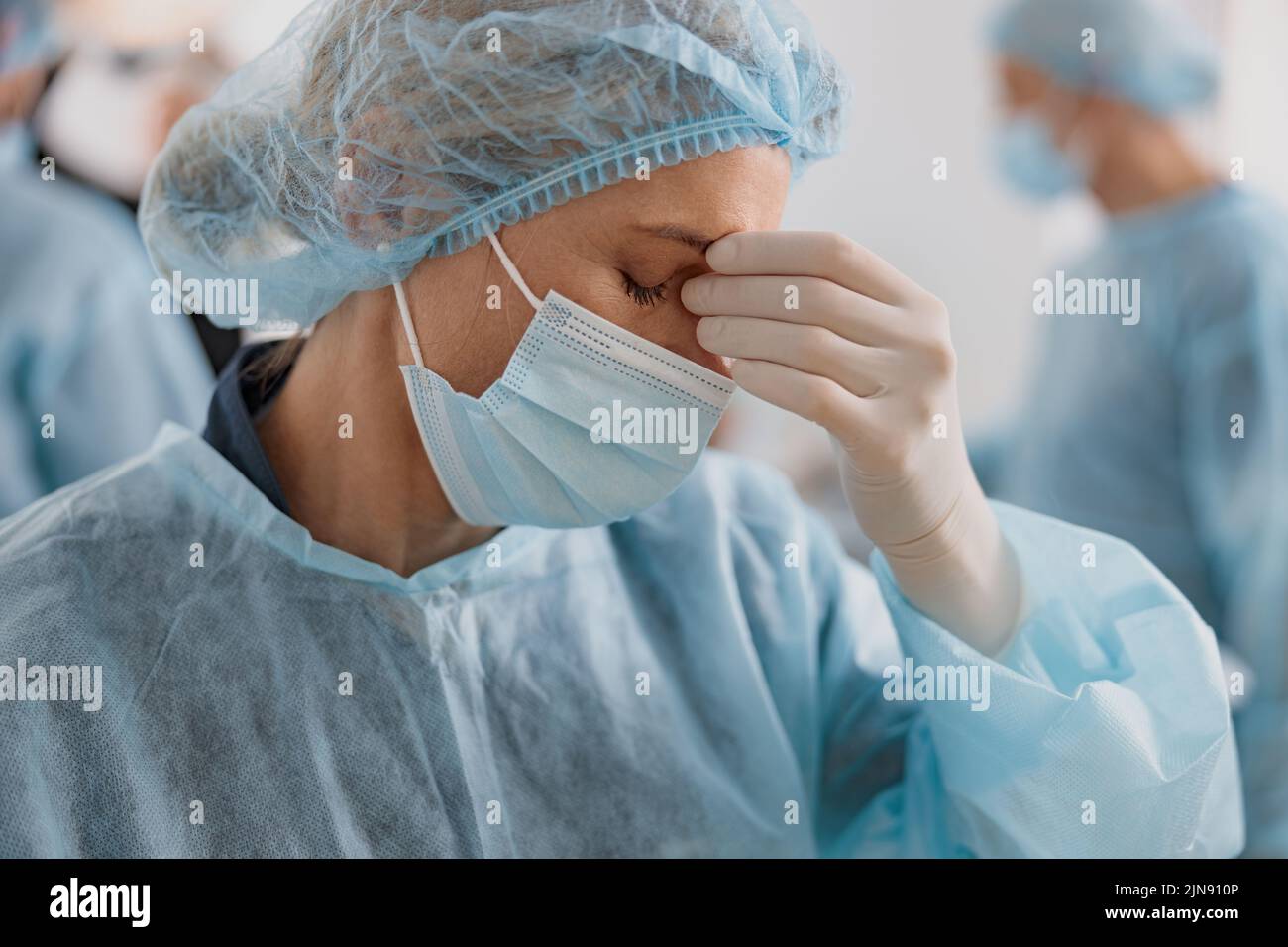Professional tired surgeon in mask standing in operating room after major surgery Stock Photo