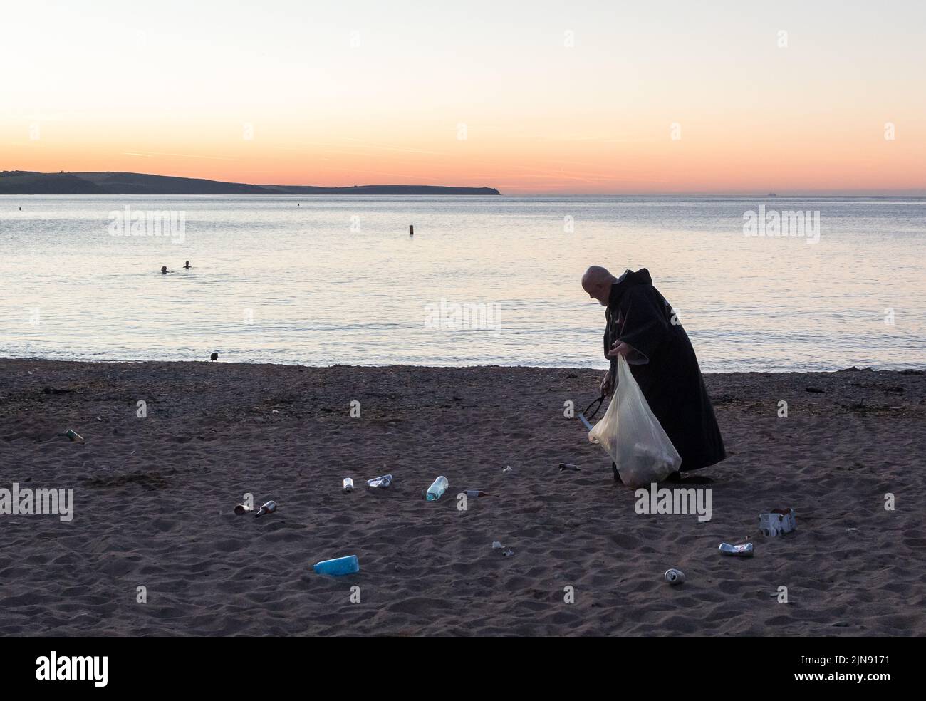 Myrtleville, Cork, Ireland. 10th August, 2022. Before sunrise the Very Rev. Patrick Stevenson, Parish Priest of St. Brigid’s Church Crosshaven walks along the strand collecting bottles, cans and other rubbish which have been discarded  by visitors to Myrtleville beach, Co. Cork, Ireland.  - Credit; David Creedon / Alamy Live News Stock Photo