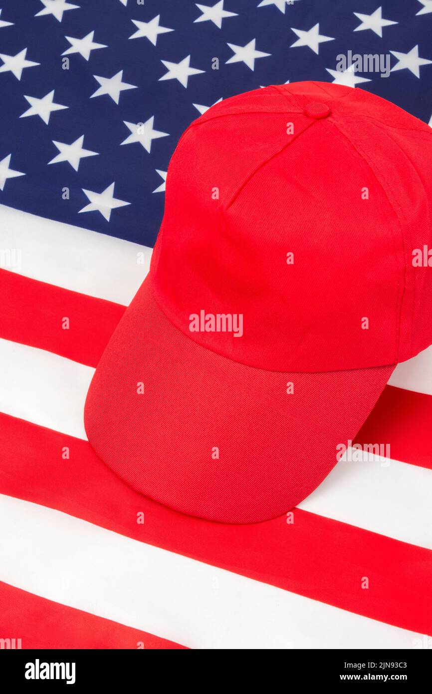 Red MAGA-type hat with blank front caption area on US Stars and Stripes flag. For Republicans in 2024 elections, American elections, US red wave. Stock Photo