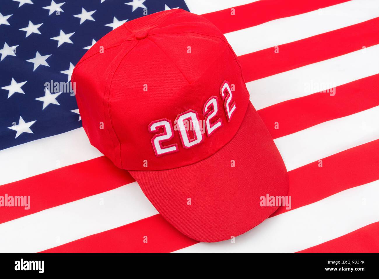 Red MAGA-type hat with 2022 date on US Stars and Stripes flag. For Republican wins in 2022 US Midterm elections in November & US Republican Red Wave Stock Photo