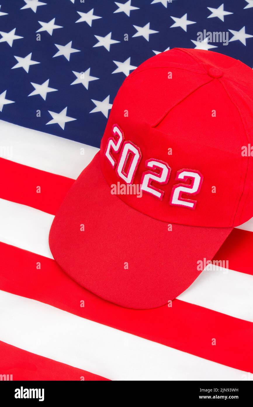 Red MAGA-type hat with 2022 date on US Stars and Stripes flag. For Republican wins in 2022 US Midterm elections in November & US Republican Red Wave Stock Photo