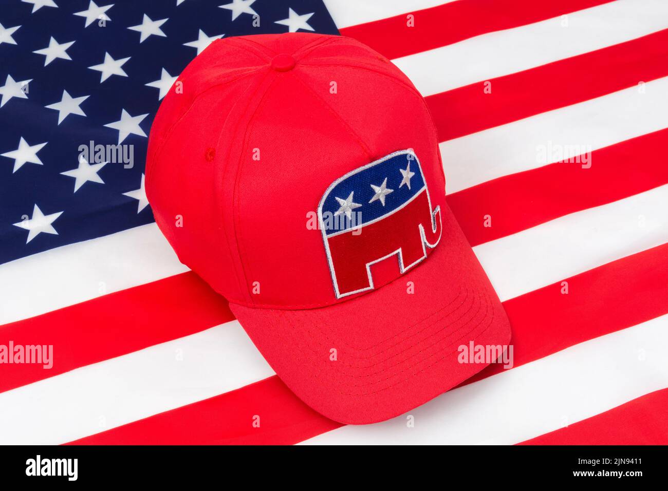 Red MAGA-type cap & Republican Elephant logo & US Stars and Stripes backdrop flag. For 2024 US Presidential election in November & Republican Red Wave Stock Photo