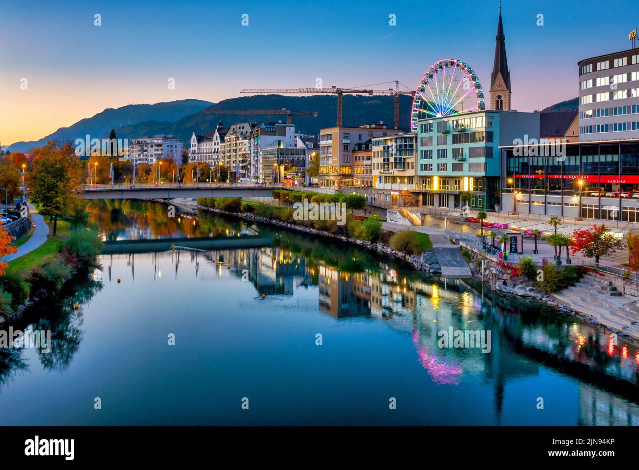 View of the bank of the river Drau with the ferris wheel and the bell tower of the Nikolaikirche; Villach, Austria Stock Photo