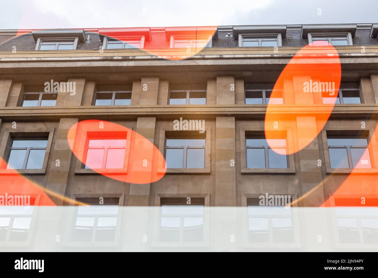 Reflection of a building in a window decorated with large orange ovals Stock Photo