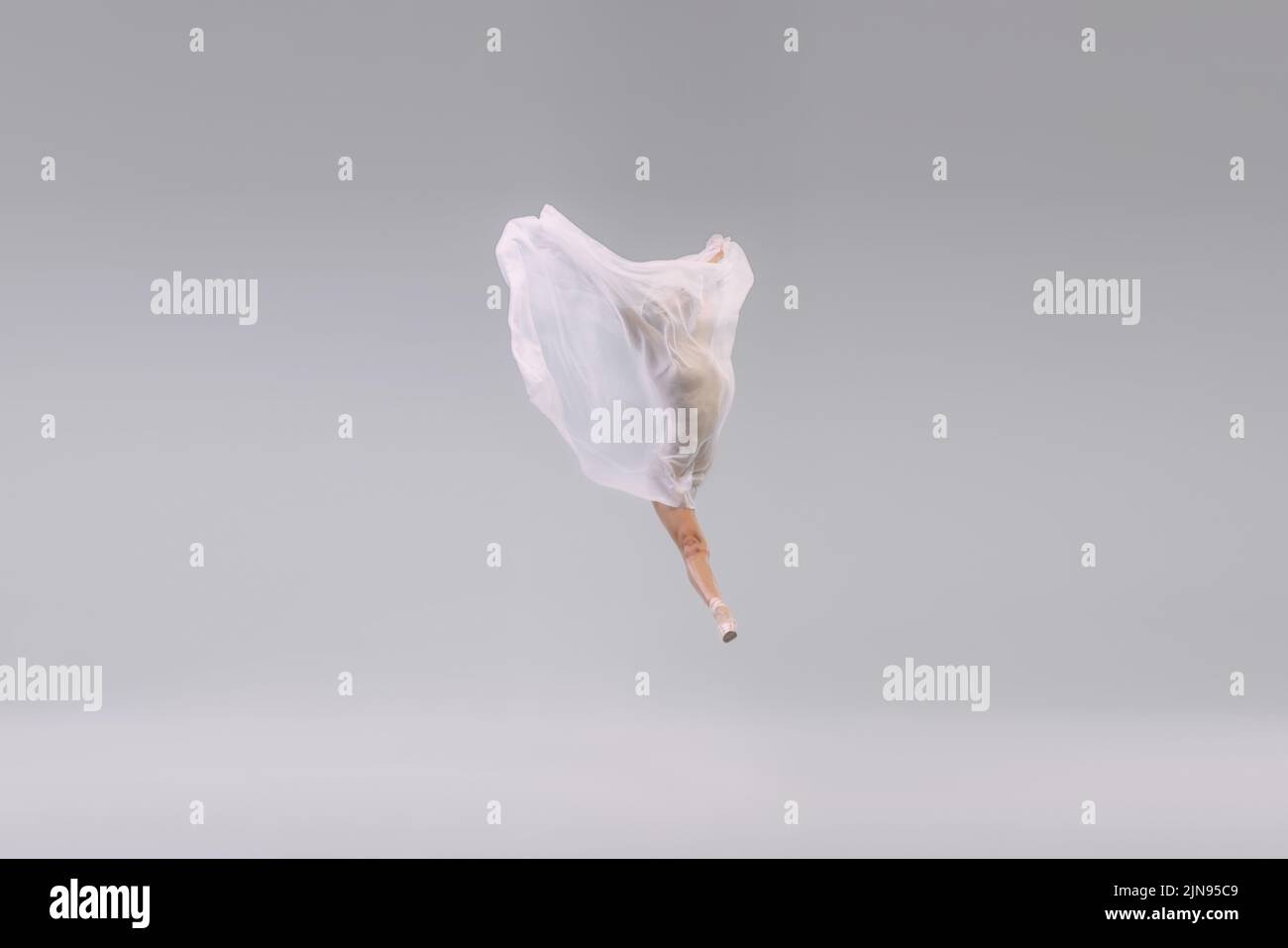 Portrait of young ballerina dancing, performing with transparent with fabric isolated over grey studio background. Weightlessness Stock Photo
