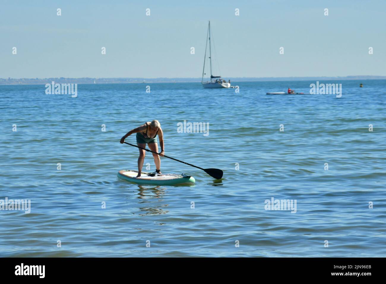 Studland Beach, Shell Bay, Dorset, UK, 10th August 2022, Weather. Hot and sunny at the beginning of another heatwave. A woman finds her balance on a paddleboard. Credit: Paul Biggins/Alamy Live News Stock Photo