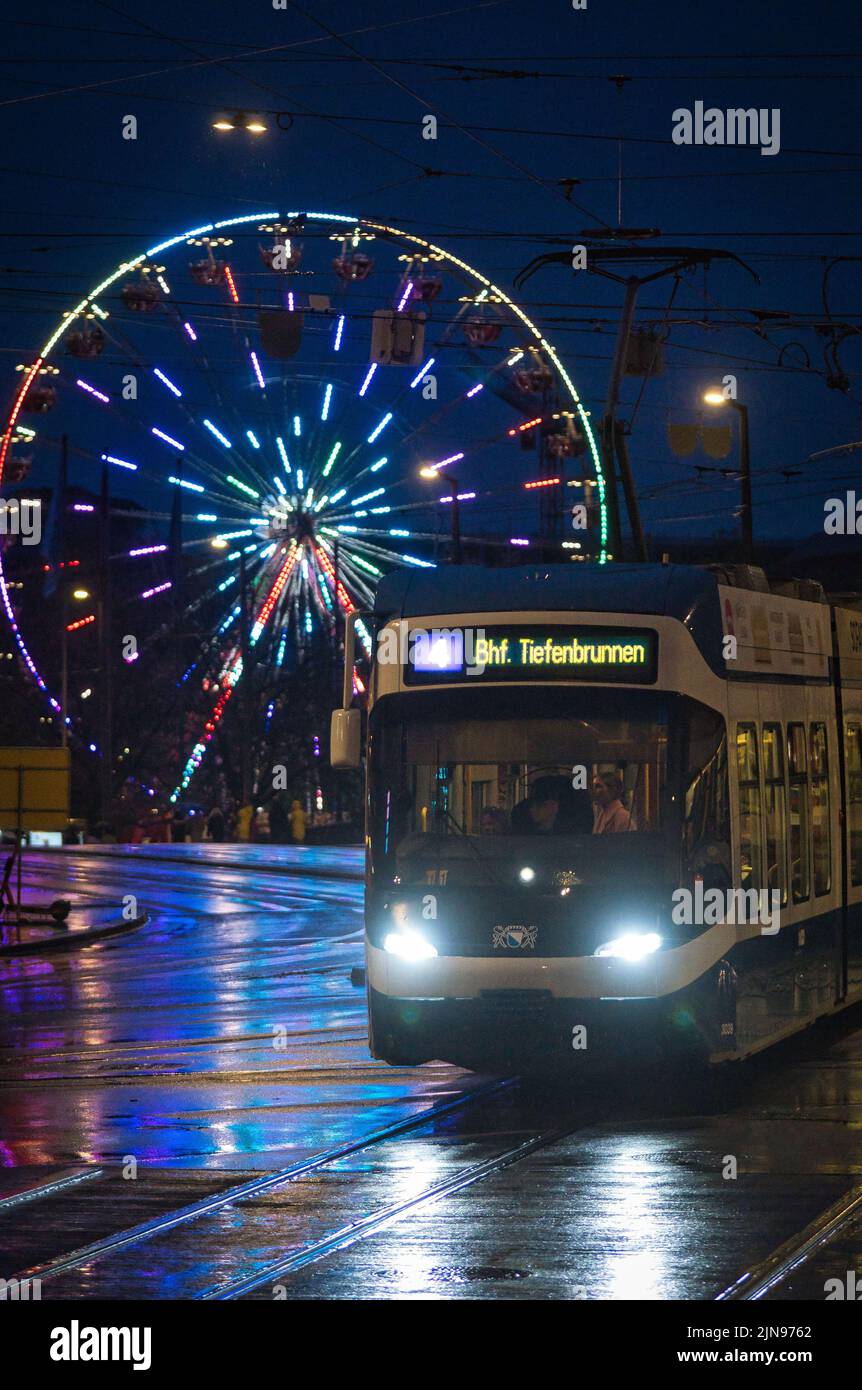 A vertical shot of a tram with a Ferris Wheel in the background on a rainy night. Zurich, Switzerland. Stock Photo